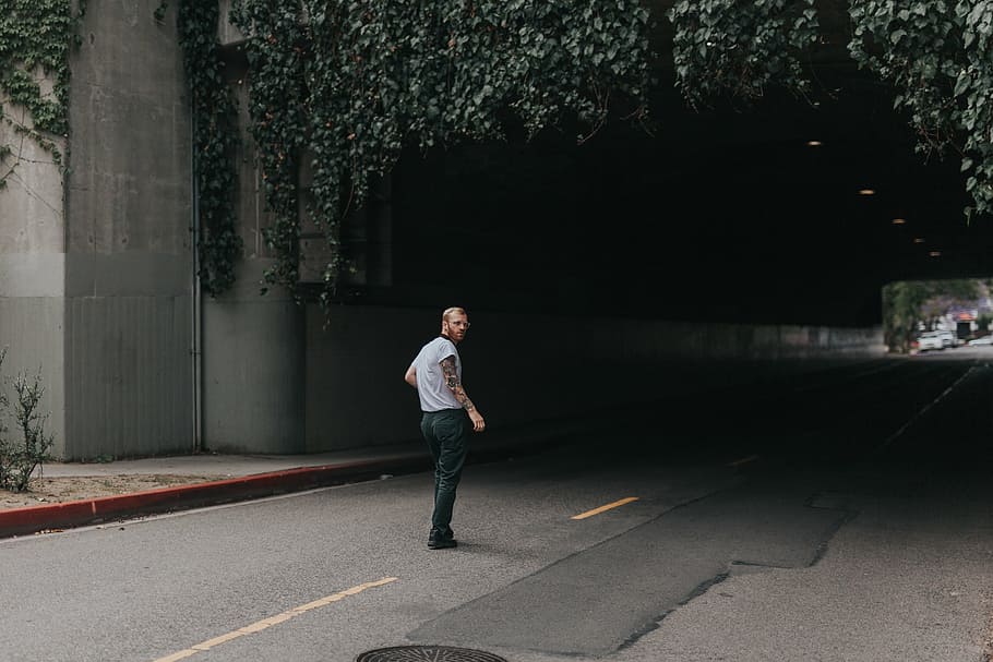 man in shirt stands near road tunnel with green vines at daytime HD wallpaper