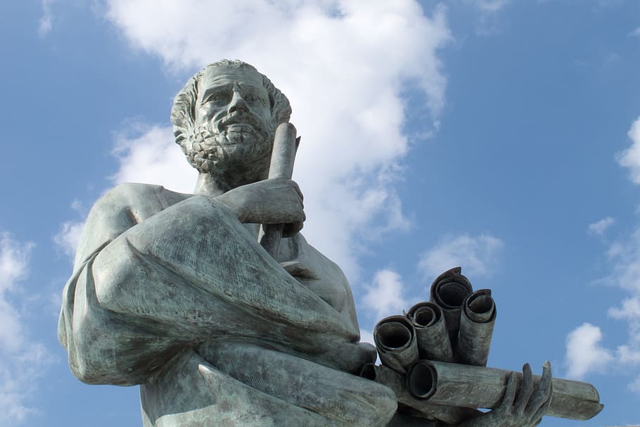 low angle photo of man holding scroll grey statue during cloudy day