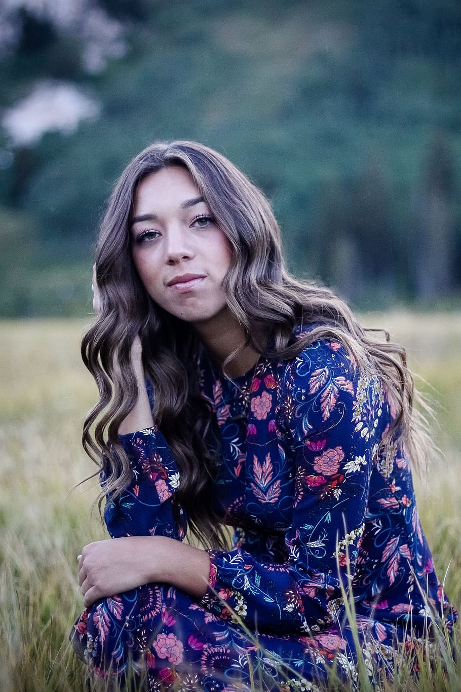 selective focus photo of woman sitting beside grass and wearing blue and white floral dress, woman sitting in middle of grass field while posing HD wallpaper