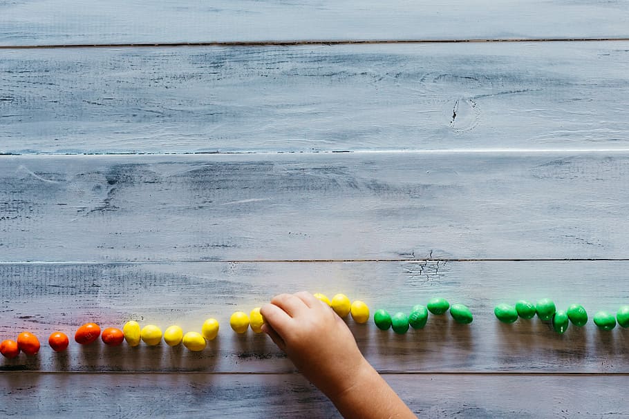 child filing red, yellow, and green candies, bead lot on board HD wallpaper