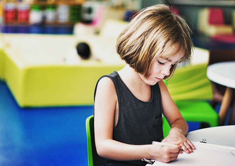 shallow focus photography of girl sitting on chair drawing on her paper on top of the table, girl sitting in chair while writing on paper HD wallpaper