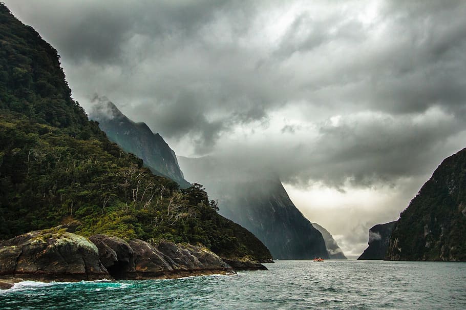 green mountains by the sea under gray clouds during daytime HD wallpaper