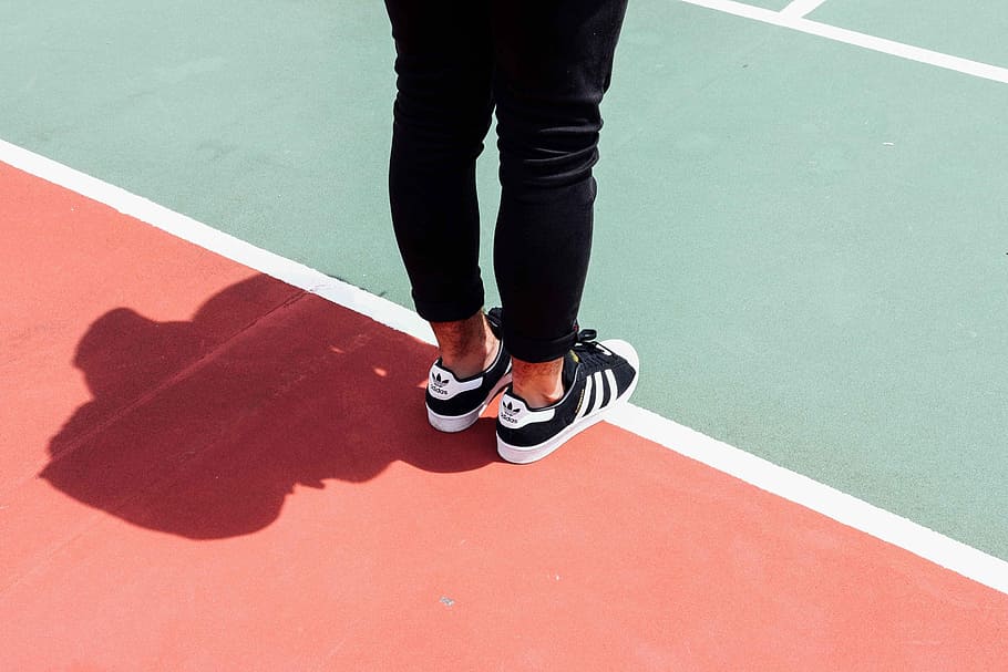 person wearing black adidas sneakers, person standing on track field