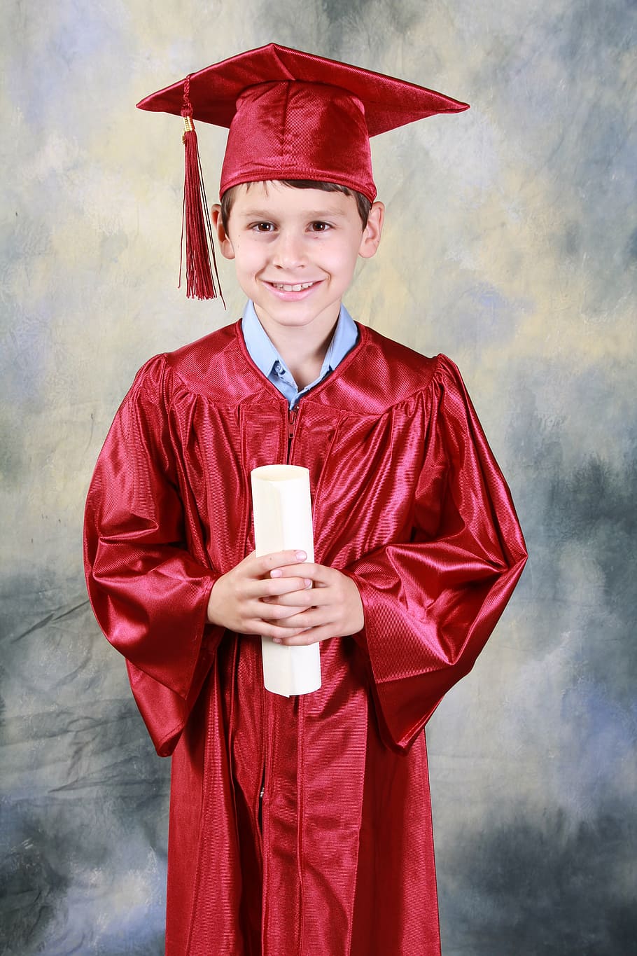 smiling boy wearing red academic dress holding diploma, graduation