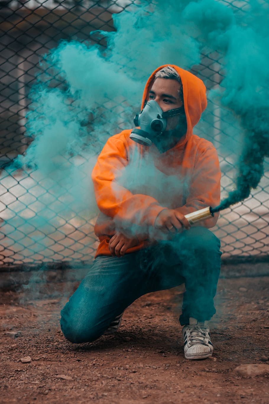 man holding tube with green smoke during daytime photo, person wearing respirator mask while holding green smoke bomb