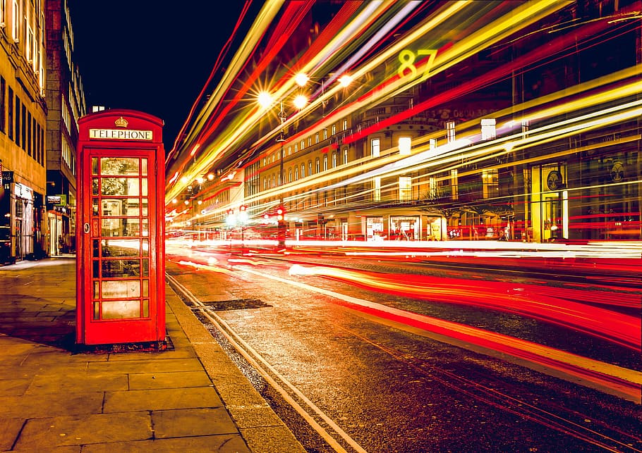 red telephone booth on concrete ground near buildings at nighttime HD wallpaper