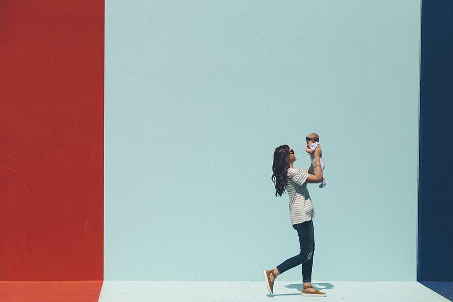 woman carrying baby while walking, woman carrying baby beside wall
