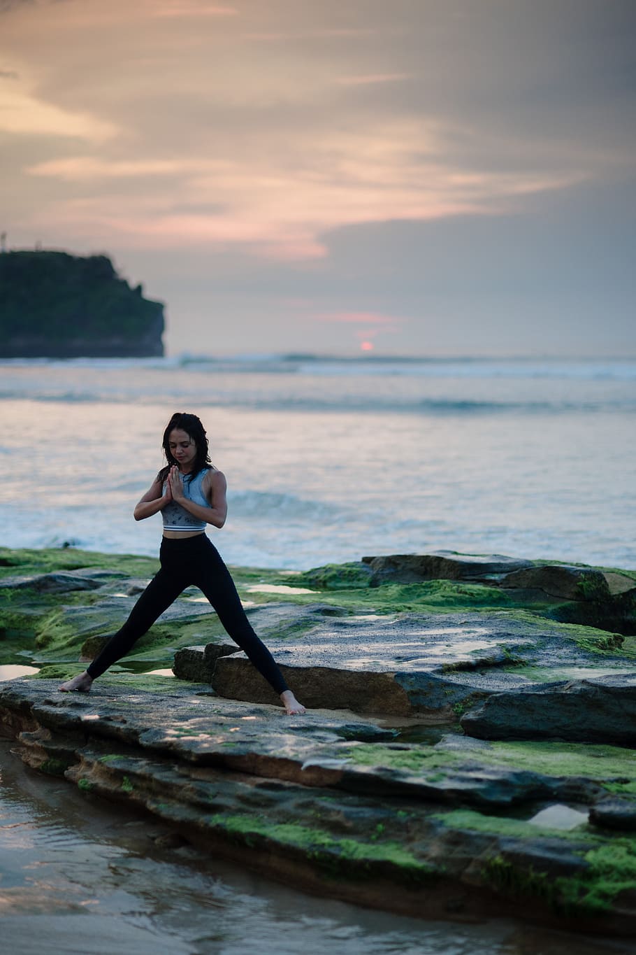 woman doing yoga on rock platform next to body of water, woman doing yoga beside sea under clear blue sky during daytime