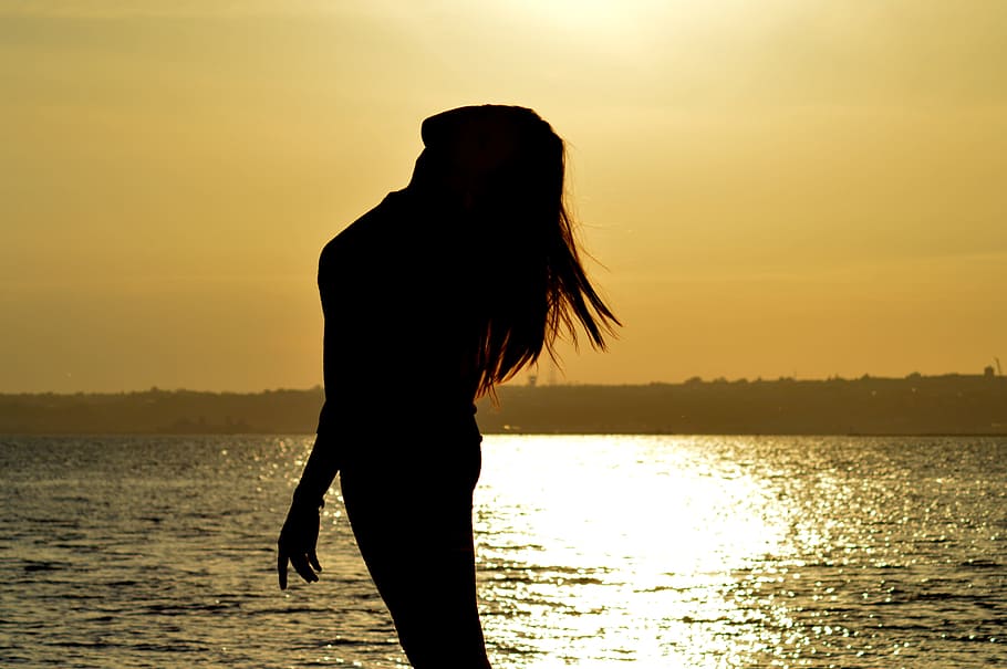 woman standing near body of water during sun set, silhouette
