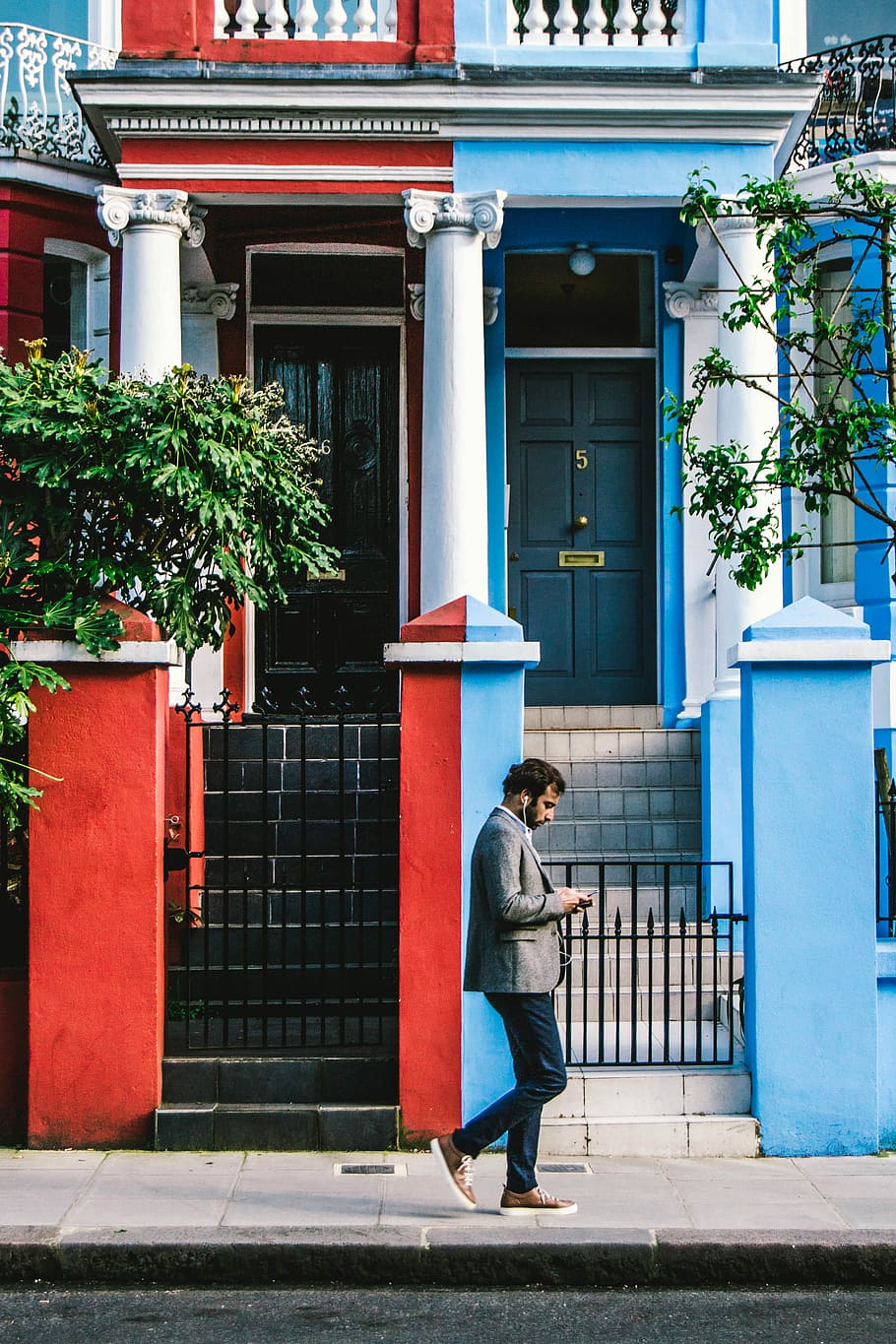 man using smartphone passing by blue and red houses, man walking front of blue and red house