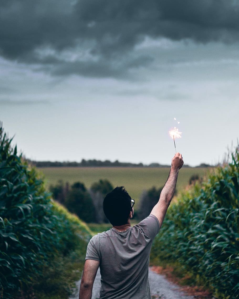 man standing on pathway holding sparkler, man lifting sparkler facing grass field HD wallpaper