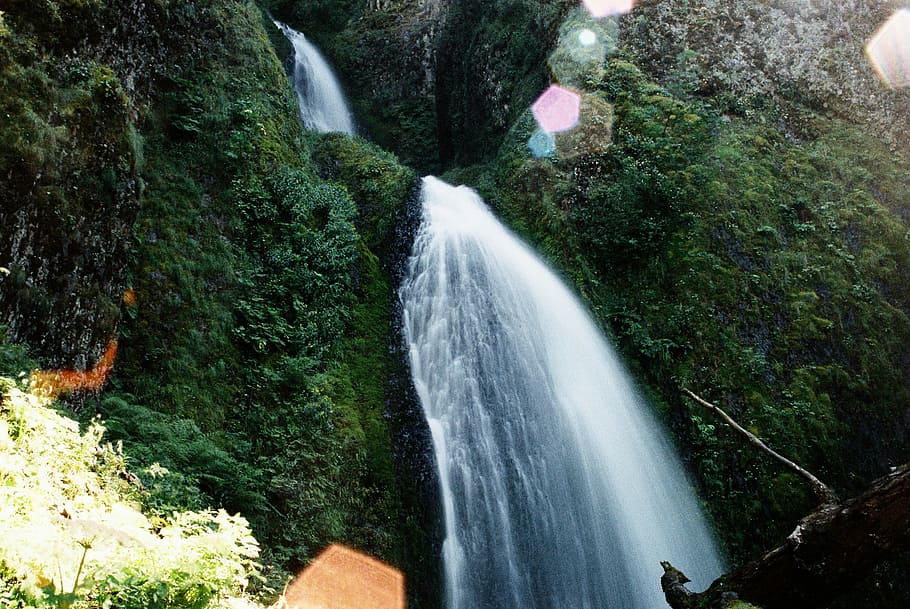 waterfalls in between mountain covered with green plant s, low angle photo of waterfall taken at daytime HD wallpaper