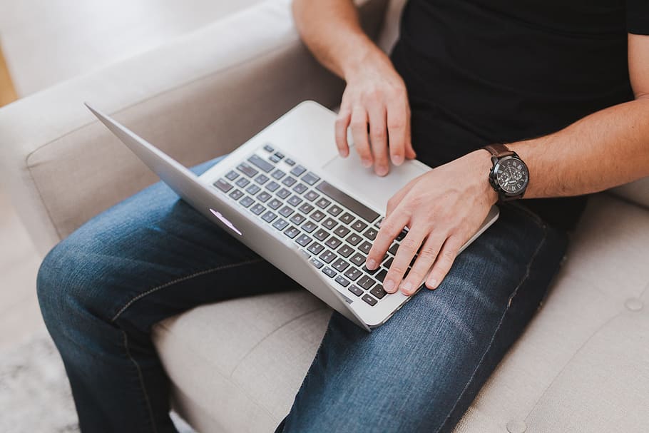 man wearing black shirt and blue denim jeans with MacBook Air on lap HD wallpaper