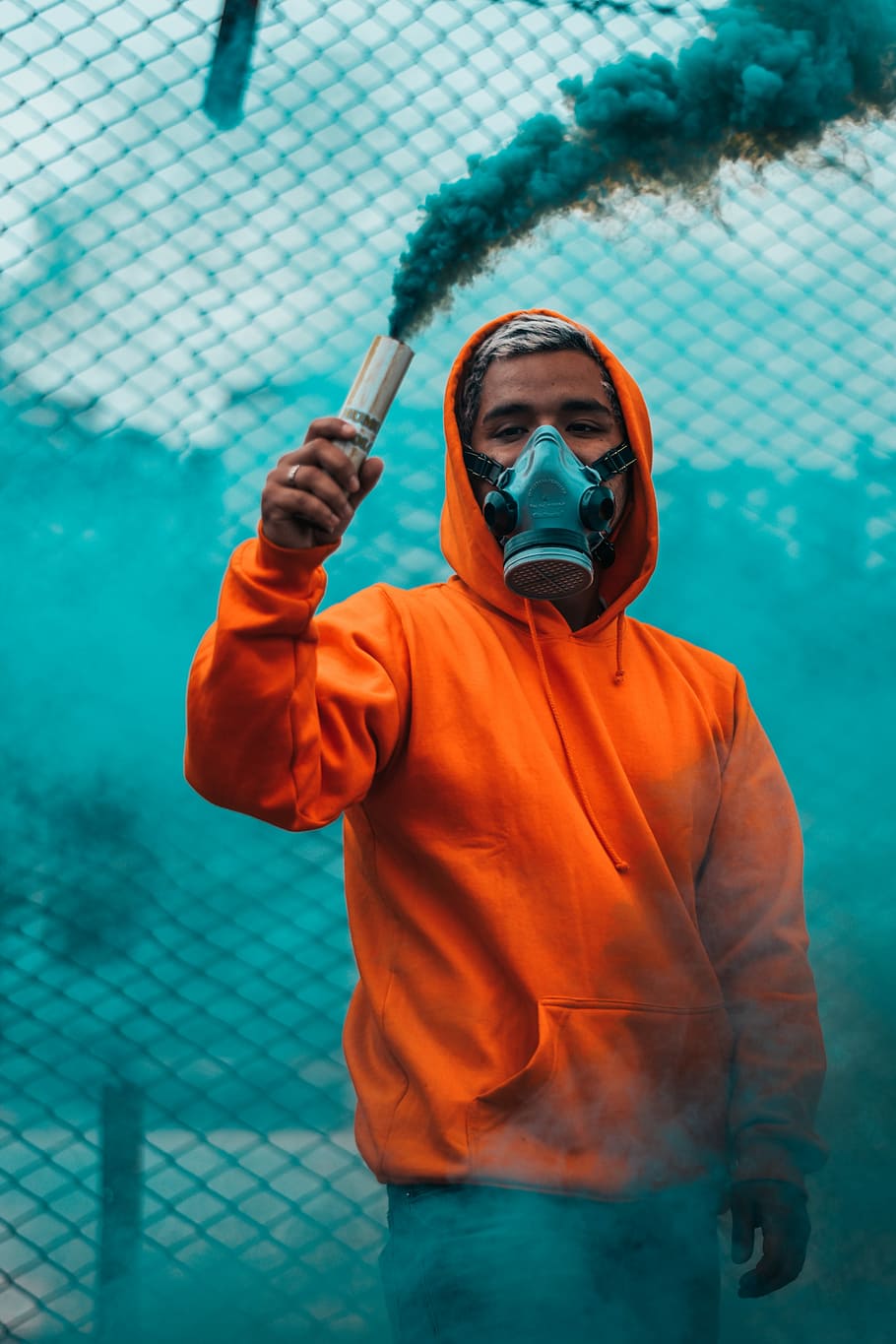 man wearing orange pullover hoodie holding smoke flare, man with gas mask holding blue smoke flare, HD wallpaper