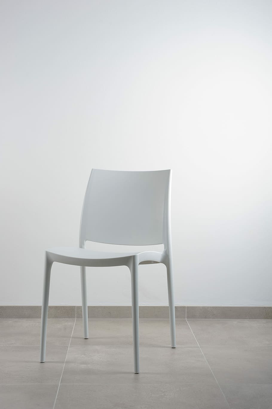 white armless chair near white wall, white chair in front of white wall