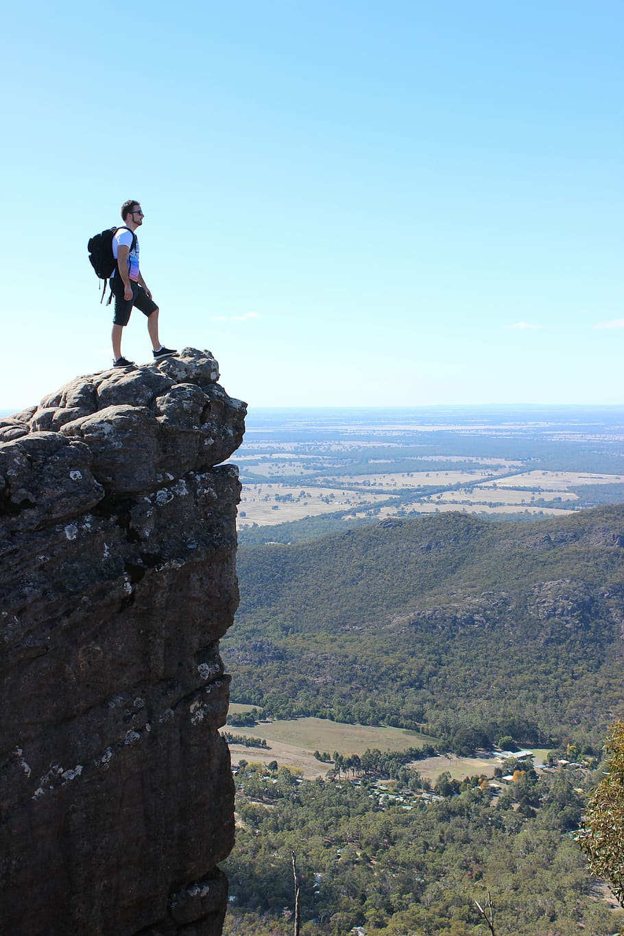 man standing on rock mountain cliff during daytime, backpack HD wallpaper