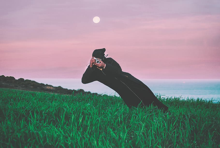 person talking photo in t he middle of grass field, person holding camera on green grass HD wallpaper