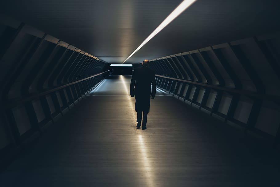 person wearing black long-sleeved shirt walking on tunnel, man in black coat standing at hallway between metal wall