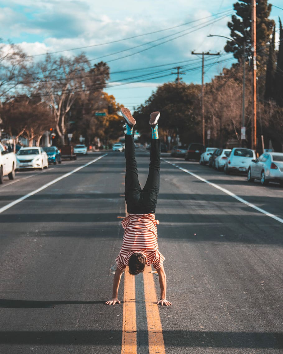 man doing hands stand on asphalt road between trees, man doing hand stand at the center of the road HD wallpaper