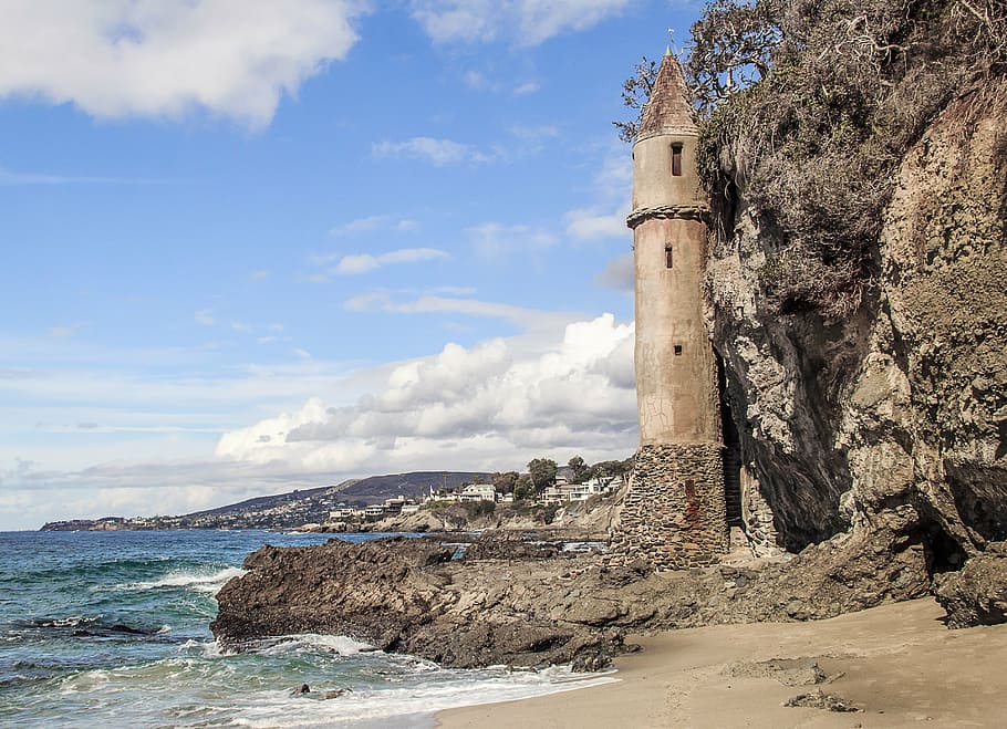 brown concrete lighthouse near body of water under blue and white sky HD wallpaper