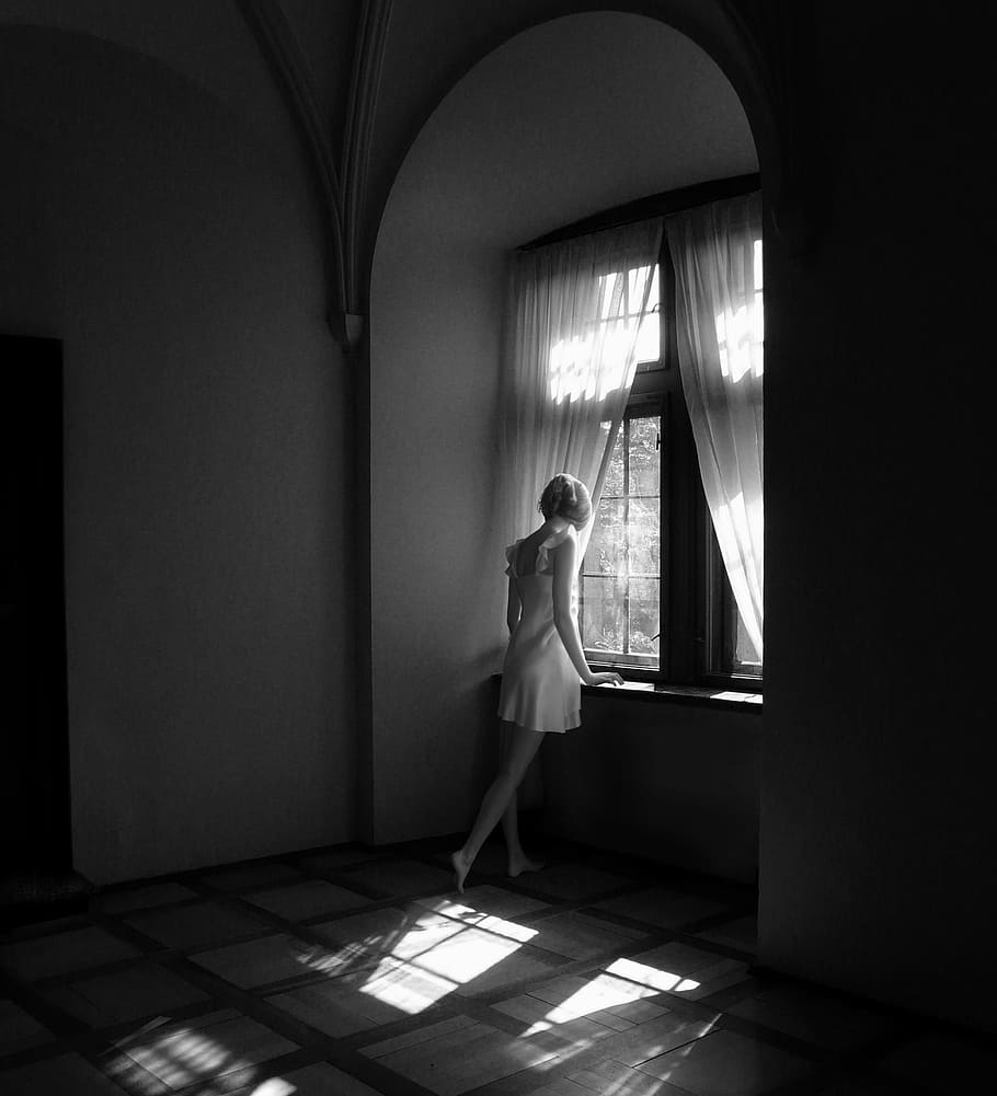 woman wearing white dress beside window and curtain, black and white