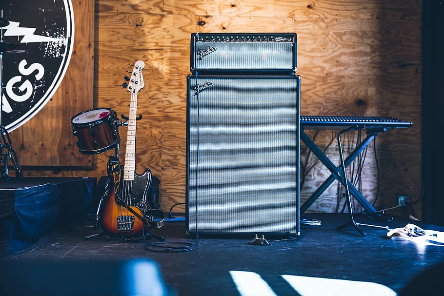 grey and black PA speakers near electric guitar and drum, stratocaster guitar beside two gray amplifiers and electronic keyboard inside brown wooden room