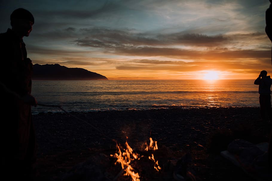 silhouette of person standing near bonfire, silhouette photography of man standing beside body of water HD wallpaper
