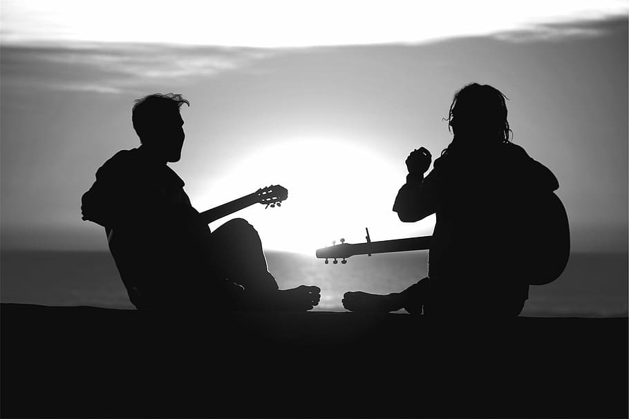 silhouette photography of two men playing guitar near body of water