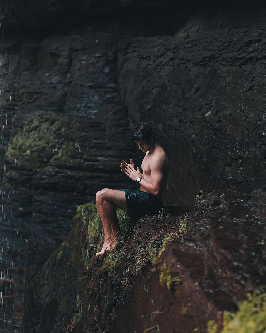 resting behind waterfall, man sitting on brown mountain, rock HD wallpaper
