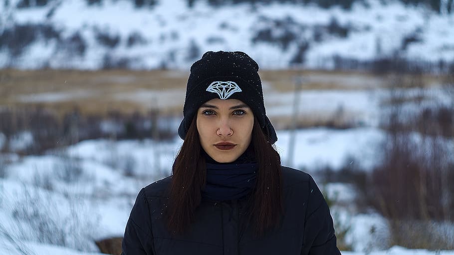 selective focus photography of woman wearing black Diamond Supply Co. knit cap and black knit sweater standing on snow covered ground at daytime