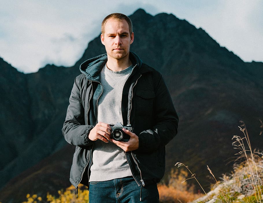 man holding camera, man in black zip-up hoodie holding camera HD wallpaper