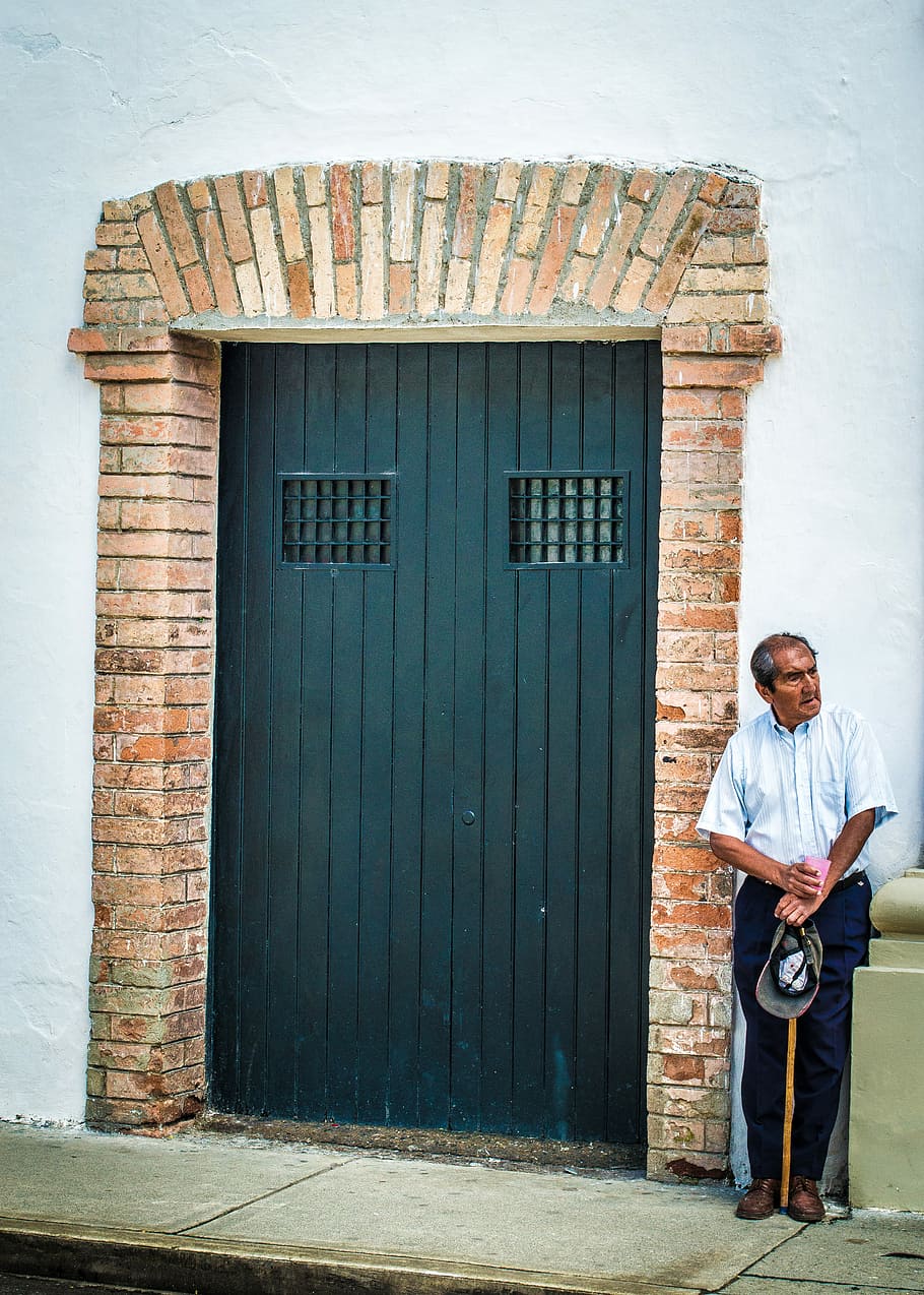 man in white shirt standing next to wooden door, man standing beside black steel gate