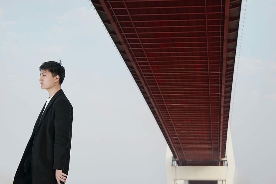 man standing under brown bridge, man wearing black coat standing under bridge during daytime, HD wallpaper