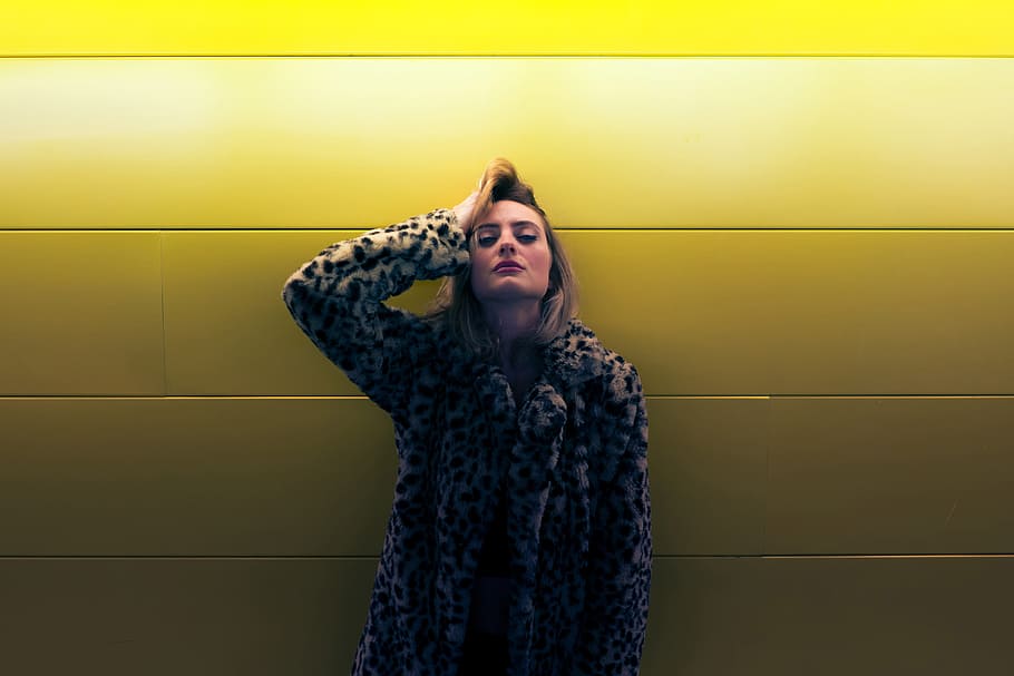 Woman wearing a coat standing by a yellow wall, people, fashion