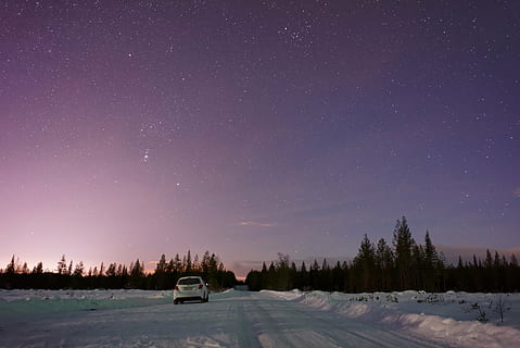 white vehicle traveling on snowy road near tree under starry skies HD wallpaper