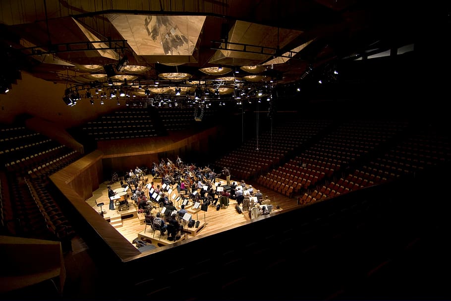 people on theater hall, orchestra practicing on stage surrounded by benches and chairs inside building with professional lighting, HD wallpaper