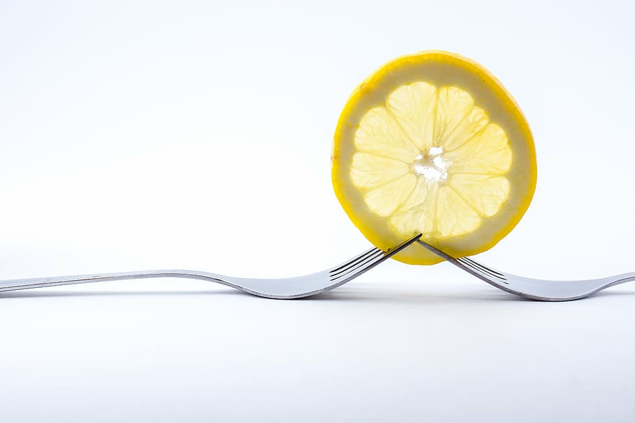 two forks piercing lemon slice on white surface, cutlery, eat