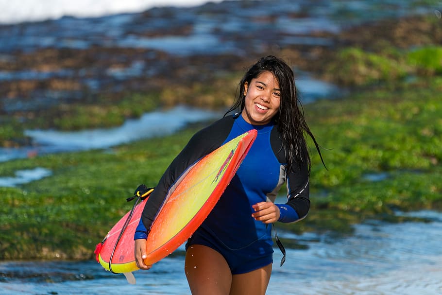 smiling woman carrying surfboard during daytime, woman holding surfboard, HD wallpaper