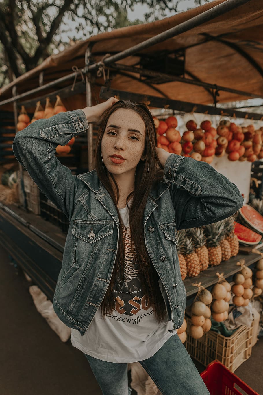 woman standing in front of fruit stand selective focus photography, woman in blue denim jacket standing in front of fruit display