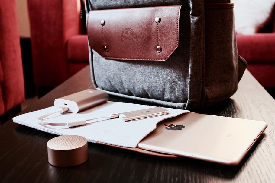 silver power bank beside bag and iPad on brown wooden table, cafe