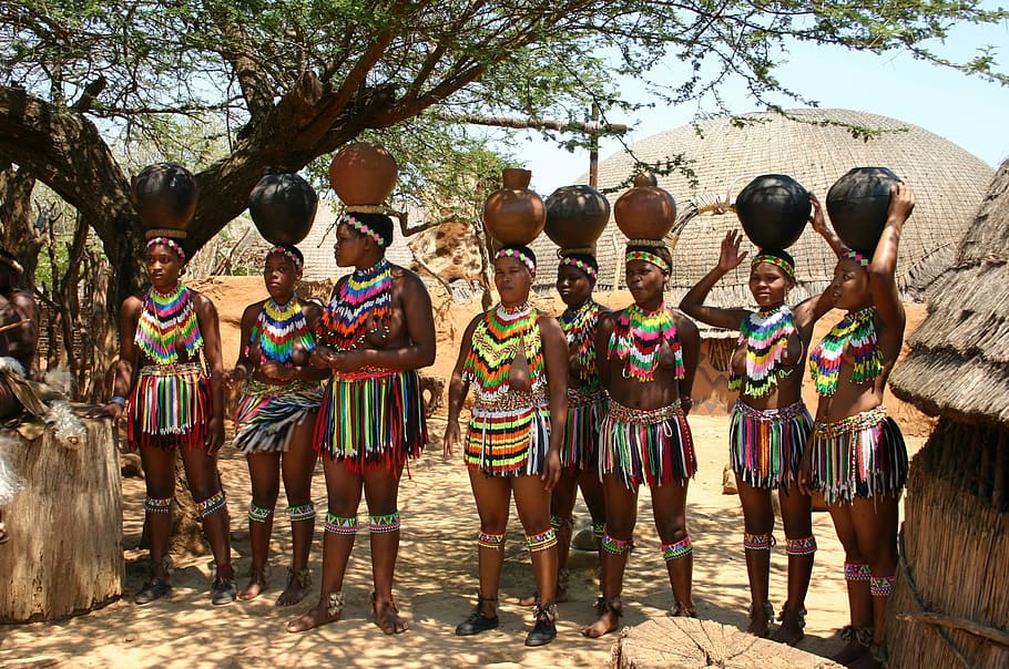 group of women wearing multicolored tops and skirts standing with pots on heads