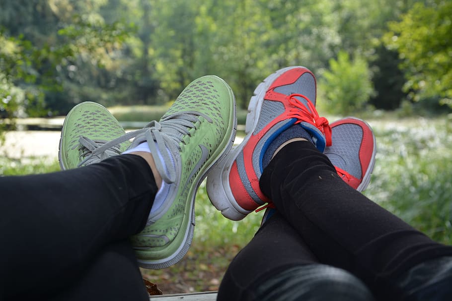 two person showing pair of low-top sneakers near trees and grass during daytime