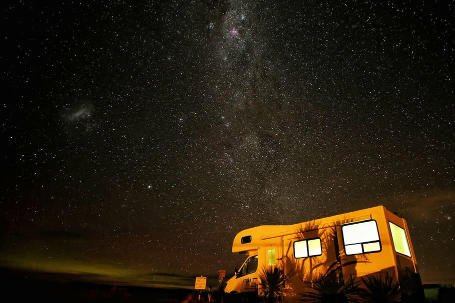 brown recreational vehicle parked near plants during nighttime HD wallpaper
