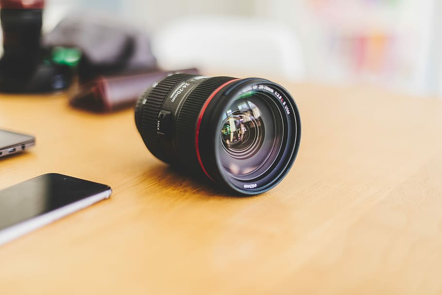 black camera lens on desk beside smartphone, black camera lens HD wallpaper