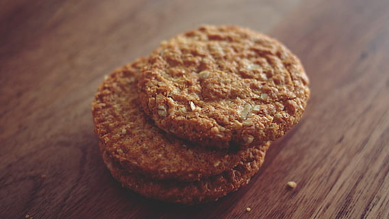 three brown cookies stacked on top of one another placed on brown wooden surface HD wallpaper