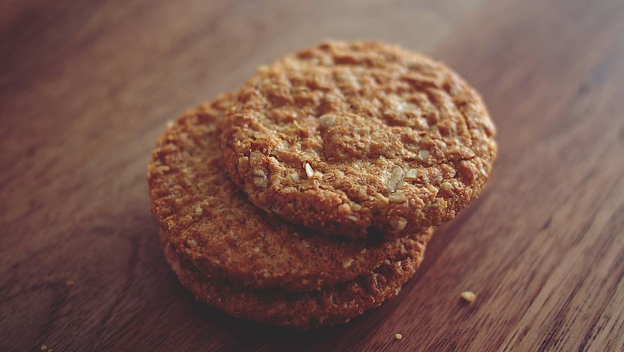 three brown cookies stacked on top of one another placed on brown wooden surface HD wallpaper