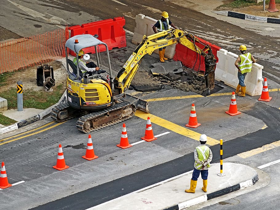 orange traffic cone on gray concrete road, excavators, construction machine