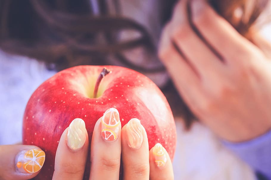 woman holding apple fruit with orange french tip accent manicure in closeup photography