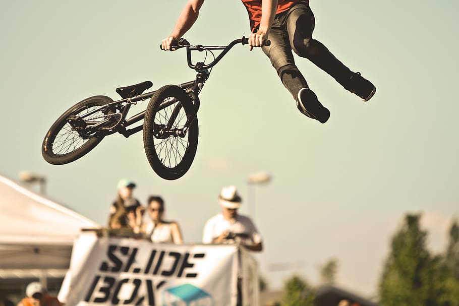 person doing BMX tricks, man performing BMX tailwhip while on air near people on top of Slide Box platform at daytime, HD wallpaper