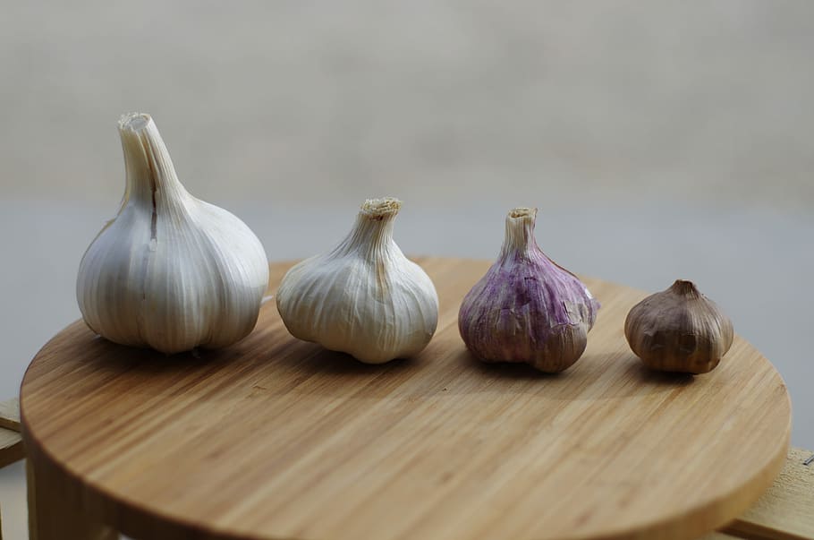 four assorted-size-and-color garlic bulbs on brown chopping board